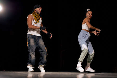 Stylish friends man and woman dancing hip-hop in casual clothes on black background at dance hall with white light. Youth culture, hip-hop, movement, style and fashion, action. Fashionable portrait.の写真素材