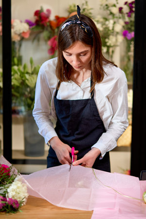 florist woman cutting envelope for bouquet decoration using scissors, in shop. beautiful female in...