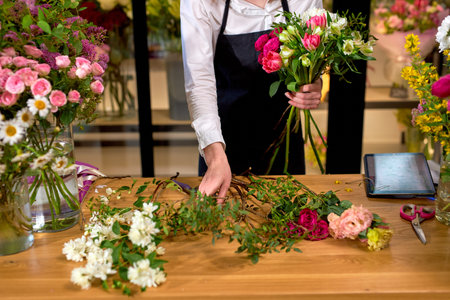 Florist at work: cropped caucasian woman arranging floral decorations, making bouquet for clients....