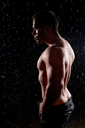 Strong and fit caucasian man bodybuilder posing at camera, standing in rain, water drops on perfect body. Sporty muscular shirtless guy with naked torso. Sport, fitness motivation. Male modelの写真素材