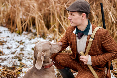 Hunting period, autumn season open. male hunter with gun in suit, in search of a trophy. caucasian man sit with weapon and hunting dog tracking down the game, sitting together.の写真素材