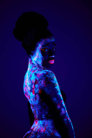 slim black fashion woman in neon UF light. attractive young model with fluorescent creative psychedelic make-up, body-art. shoot from back, side view. art, fashion, lifestyle, people conceptの写真素材