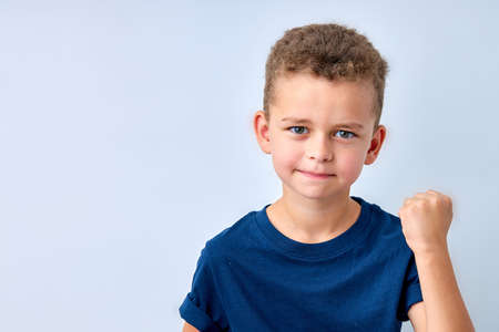 handsome boy looks angry. The child is offended, threatens, shows a fist. Angry, resentful, aggressive child. Portrait on white studio background. Childrens human emotions conceptの写真素材