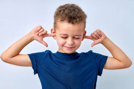caucasian little kid boy closing eyes and discontentedly closing ears with hands, irritated. nervous boy doesnt want to hear parents quarrel, ignoring the notice of mommy. isolated on whiteの写真素材