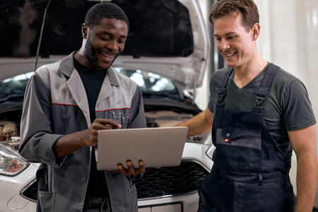 Black Car Mechanic And Caucasian Repairman Checking Diagnostics Results on Laptop, Computer....