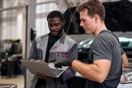Black Auto Mechanic And Caucasian Repairman Checking Diagnostics Results on Laptop, Computer....