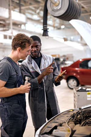 american and black Men mechanic inspection checking bug in engine from application smartphone. white car for service maintenance insurance with car engine.for transport automobile automotiveの写真素材