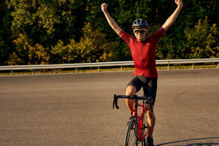 Athletic happy strong man cyclist in professional cycling garment on bicycle on road. Sportsman is raising hands up with happy cheerful smile. healthy sporty lifestyle, success, win, competitionの写真素材