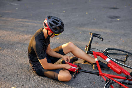young caucasian man with knee injury while cycling on forest road during the summer time, health care problem concept. unhappy man wearing helmet and suffering from knee ache,using medicine chestの写真素材
