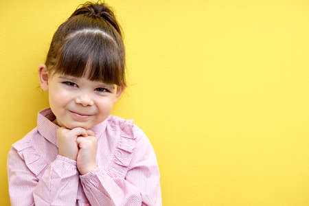 Portrait of cute child girl in pink blouse looking at camera posing, isolated on yellow studio background, sweet kid girl of caucasian appearanceの写真素材