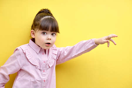 cute little kid girl scared and run expression gesture. isolated yellow background. portrait of frightened child in pink blouse looking at camera with big eyesの写真素材