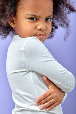 Upset unhappy angry kid girl with arms crossed, isolated on purple background. black offended child with arms folded posing at camera, with angry facial expression. children and human emotionsの写真素材