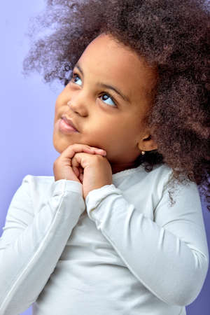 lovely cute minded pensive small child girl smiling dreamy tricky look empty space with thoughtful expression, wear white casual shirt isolated purple color background. portrait close-upの写真素材