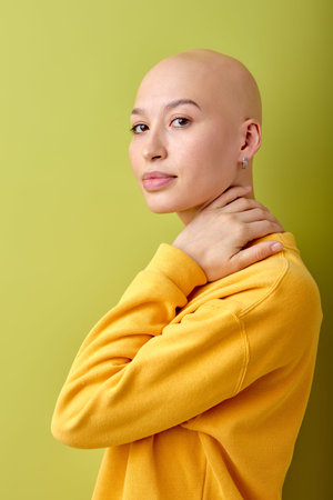 Attractive bald caucasian woman in yellow shirt standing isolated over green studio background,...