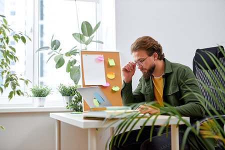 Portrait of attractive young businessman using laptop computer at office desk. paperwork and other...