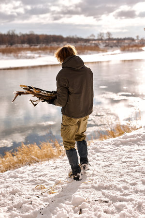 active caucasian male gathering wood for fire in forest, nature. handsome guy in warm clothes in...