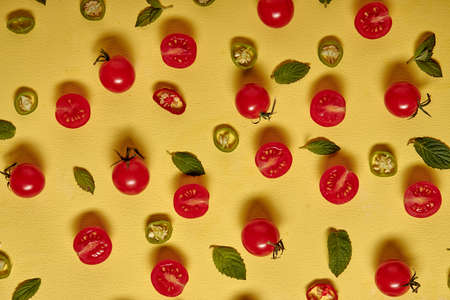 Fresh ripe cherry tomatoes slices scattered isolated on yellow background, fresh bright tomatoes with leafs, flat layの写真素材