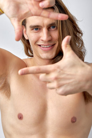 naked fit male with long hair posing at camera, half-naked man looks at camera, making shape of square like a photographer, smiling happily. isolated white studio background. close-up portraitの写真素材