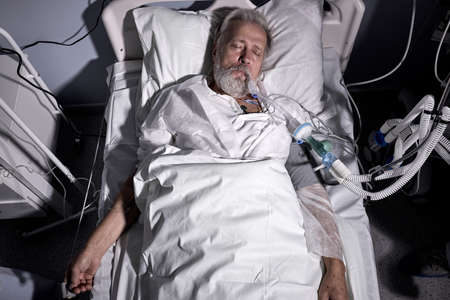 coronavirus patient with Endotracheal Tube In Mouth Lying On Medical Couch, Bed in hospital. senior sick person alone in ward room, suffering from disease. therapy, treatment, medicine. top viewの写真素材