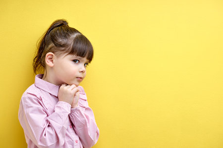 girl child thoughtfully planning an idea, thinking looking suspiciously, caucasian child isolated on yellow background, portraitの写真素材