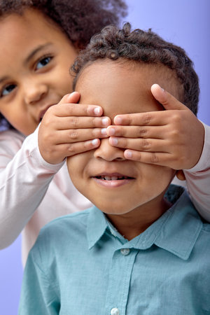 Portrait of cheerful joyful carefree little girl and boy covering eye with arms to each other and...