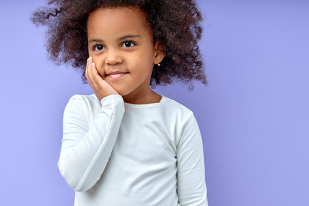 smiling black young girl kid keeps hands on cheeks,smiles satisfied,amiably, has fun chatting with friends, wears casual clothes, isolated over purple background.Good mood concept.Copy space.の写真素材