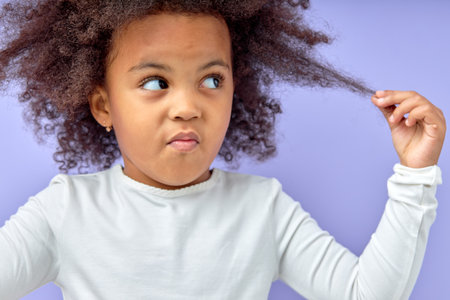 beautiful black child girl touching curly dark hair and thinking. Child portrait copy space. cunning minded look at side, at a loss. isolated on purple studio background, portraitの写真素材