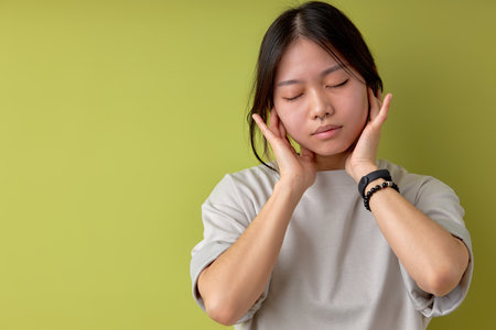 korean brunette woman listening to music in headphones, looking relaxed with eyes closed. portrait of female in casual wear enjoying music, isolated over light green studio background, copy spaceの写真素材