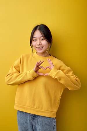 Portrait of young Beautiful attractive chinese asian woman over isolated background smiling in love showing heart symbol and shape with hands. Romantic, human emotions, people concept.の写真素材