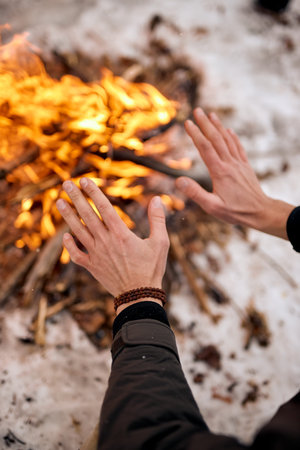 top view on male taveller warming hands by the campfire outdoors. Camping detail, travel lifestyle...