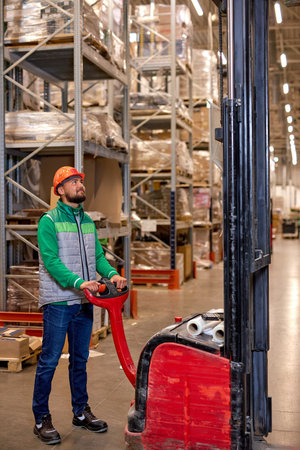 confident engineer staff male warehouse worker in hard hat working. in logistics center warehouse factory. Portrait of caucasian young worker posing with equipment loader transportの写真素材