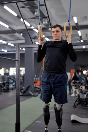 strong confident man with leg prothesis training on gymnastic rings. . Providing sport opportunities...