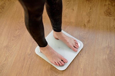 cropped unrecognizable woman in leggins stepping on floor scales indoors, sport and healthy lifestyle. Overweight problemの写真素材