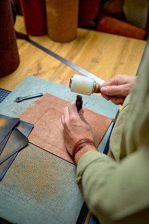 Sewing process of the leather belt. Man's hands behind sewing. Leather workshop.Making of brown...