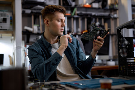 Confident caucasian repairman or engineer restores the laptop PC examining the details of parts of disassembled laptop. Electronic repair shop, technology renovation, business, concept repairs.の写真素材