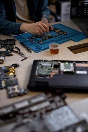 cropped male hands repairing parts in disassembled laptop using screwdriver and different tools on table in workshop. Hand technician repairing broken laptop notebook computer using toolsの写真素材