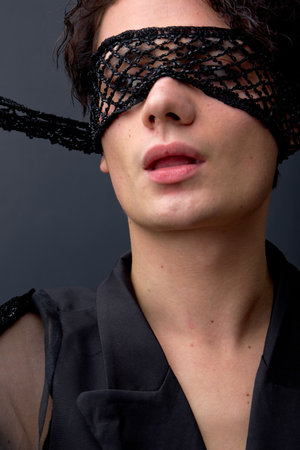Passionate male wearing semi-open eye mask posing, stylish, dressed in black jacket. brunette man lgbt member, beauty portrait isolated over black studio background. people, fashion, toleranceの写真素材