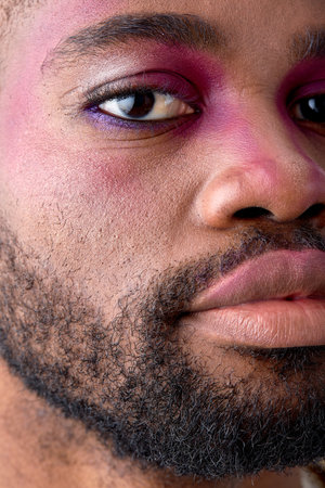 Male makeup look. close-up portrait half of black young man with pink eyeshadow make-up. black american feminine womanlike guy confidently looking at camera. models, beauty, fashion conceptの写真素材