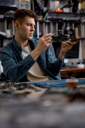 Confident professional repairman or engineer restores the laptop PC examining the details of parts...