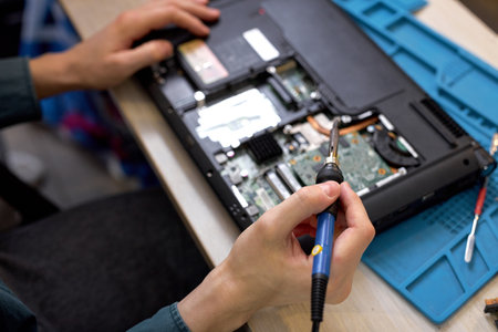 cropped male hands repairing parts in disassembled laptop using screwdriver and different tools on table in workshop. Hand technician repairing broken laptop notebook computer using tools. top viewの写真素材