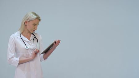 Happy and smiling young doctor typing text on the tabletの写真素材