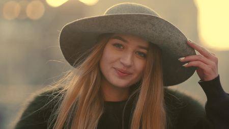 Glamorous young woman in a gray hat charmingly looks right and smile towards the cameraの写真素材