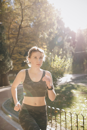 Healthy fitness athletic woman jogging outdoors. Attractive brunette female runner running in city park airpods bluetooth headphones earphones.の写真素材