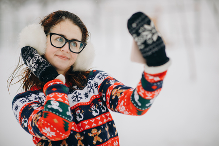 Woman makes selfie in the winter park. Smiling girl makes selfie on a background of snowy trees in a winter parkの写真素材
