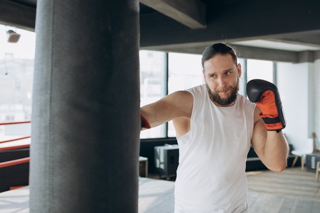 Boxer hits punching bag in gym in slow motion. Young man training indoors. Strong athlete in gym. Sport conceptの写真素材