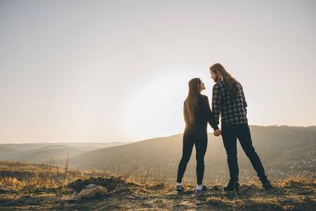 Silhouette of a female and male holding hands at sunset. Couple holding hands. Couple of lover holding hand with sunrise. Young couple kissing on the background of a sunset in the field.の写真素材