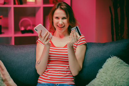 woman are buying online with a credit card while sitting on the sofa in the living room. Women are...
