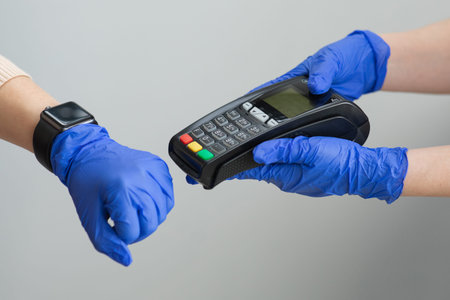 Womans hand in gloves using smartwatch to purchase product at the point of sale terminal in a retail...