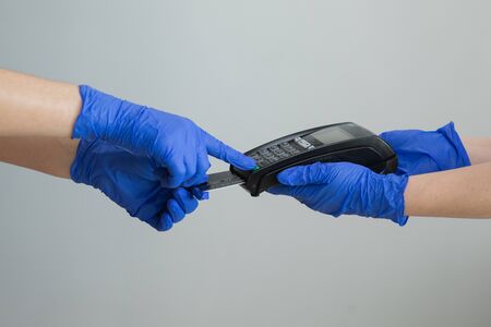 Womans hand in gloves with credit card swipe through pos terminal and enter pin code. Banking services of electronic money. Financial success and safety. Credit card machine for money transaction.の写真素材