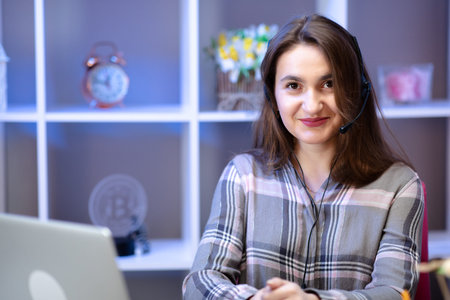Young woman using laptop computer at home, wearing headset.